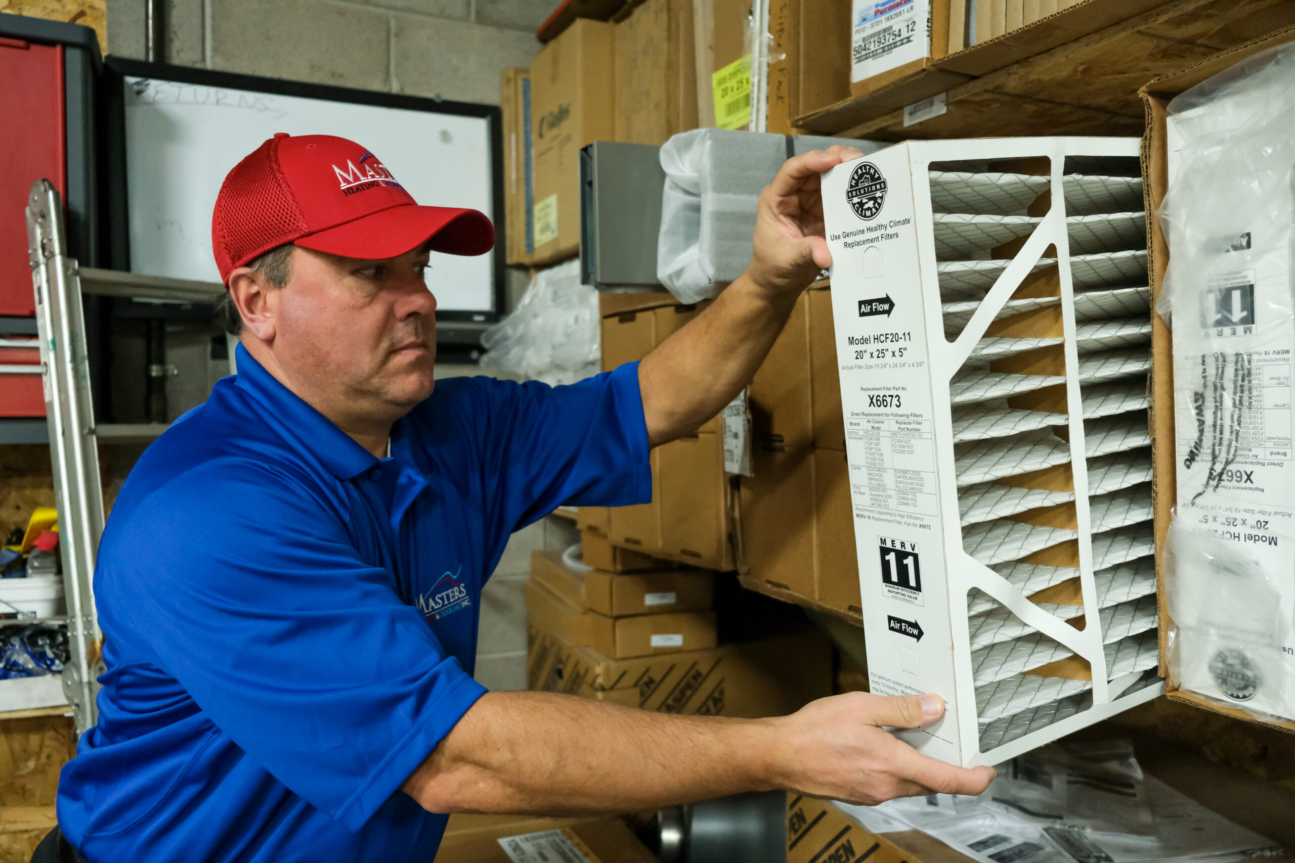 Masters Heating & Cooling technician preparing for an AC repair service appointment by getting a new air filter off the shelf