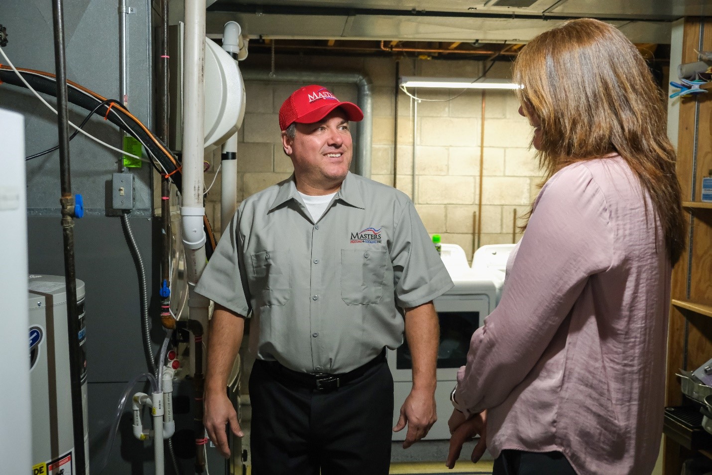 Masters Heating & Cooling technician speaking with a homeowner in front of their home’s water heater.